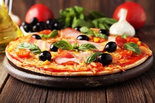 un tagliere di una pizza con sopra delle olive e del  basilico ed del prosciutto