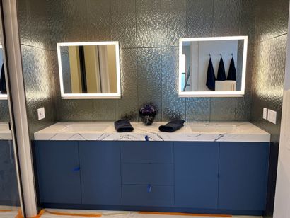 Bathroom with blue vanity, white countertop, two square mirrors, and textured wall.