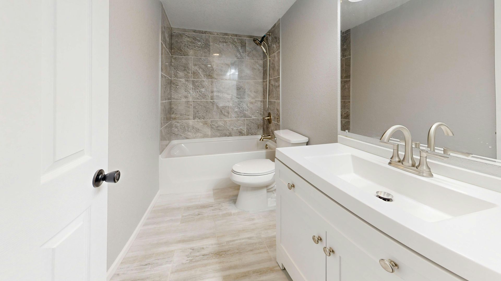 Bathroom with white vanity, toilet, and bathtub with gray marble-look shower surround.