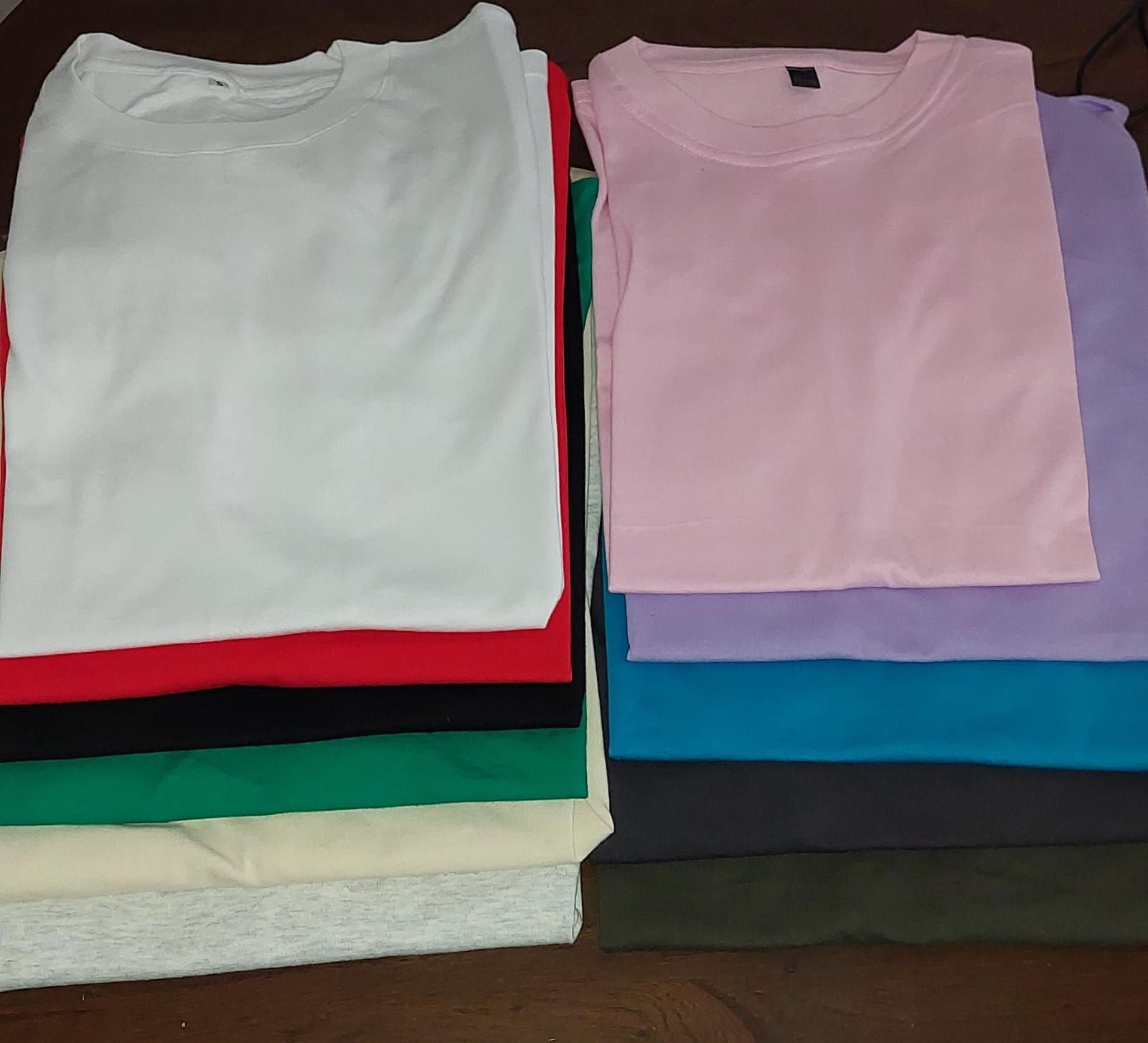 Pilas de camisetas dobladas en varios colores: blanco, rojo, verde, rosa, morado y azul.