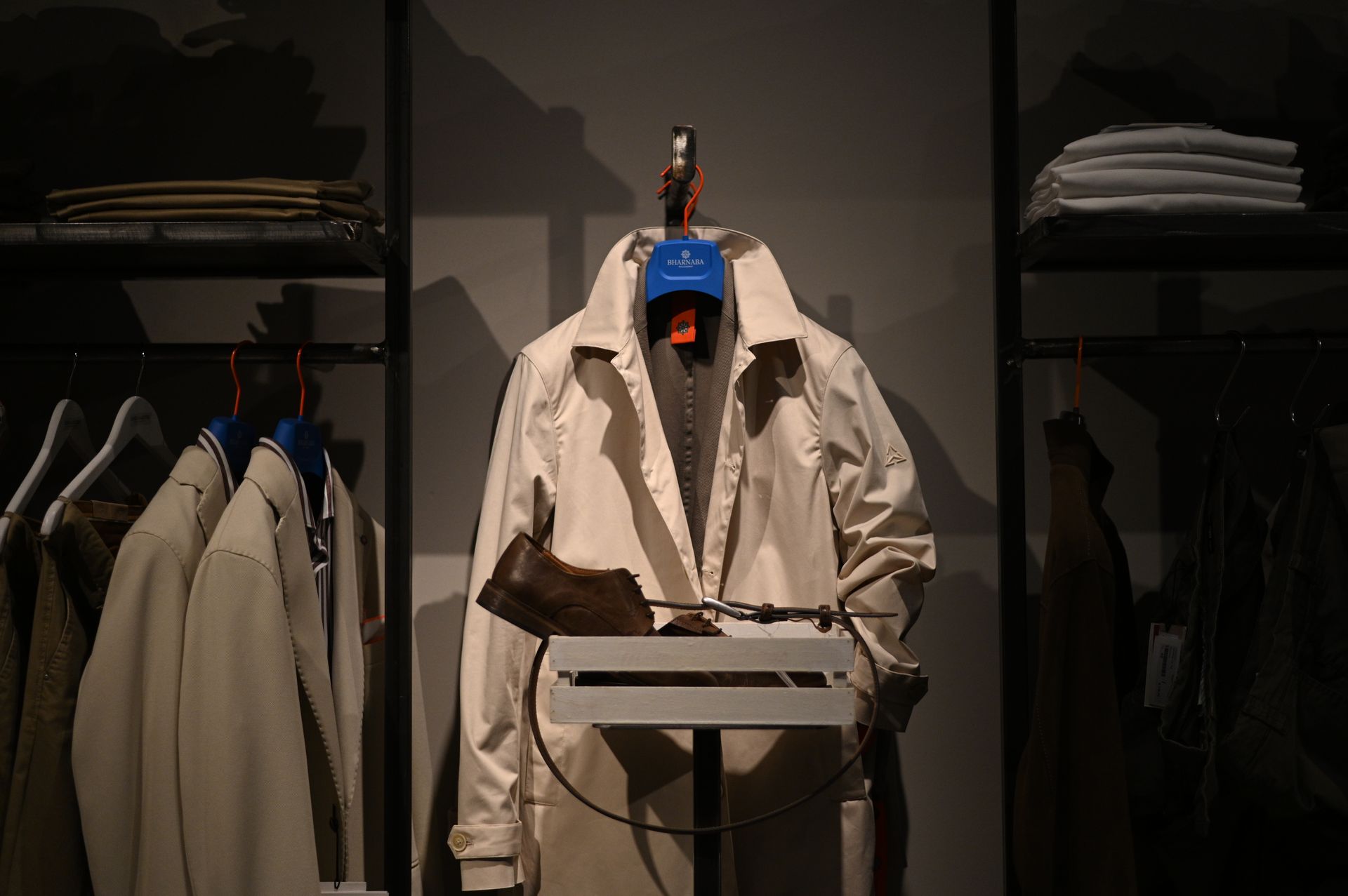 Esposizione di abiti in un negozio, con un cappotto color crema, un cappello e un espositore.