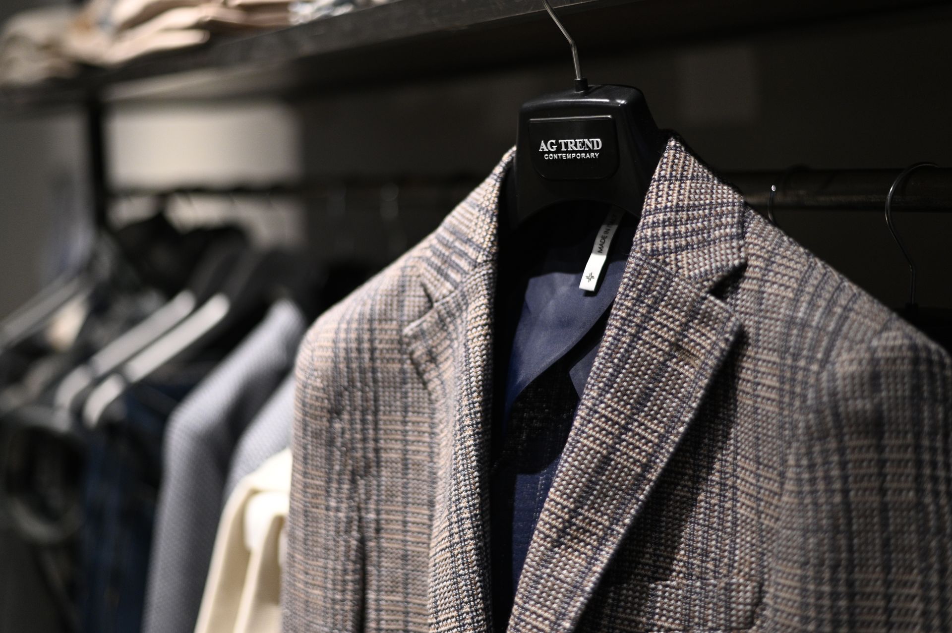 Primo piano di una giacca scozzese su una gruccia in un negozio di abbigliamento, con altri capi sfocati sullo sfondo.