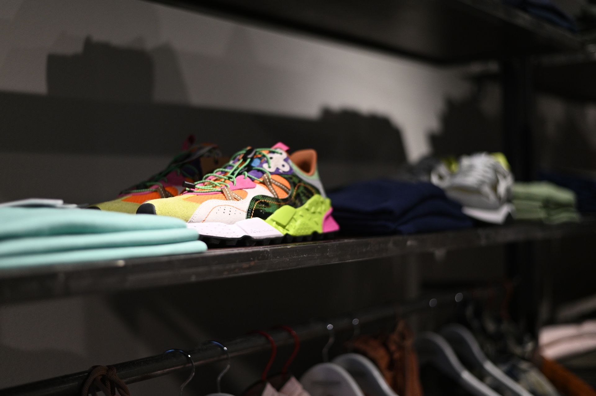 Scarpe da ginnastica con design colorato esposte sullo scaffale di un negozio insieme ai vestiti.