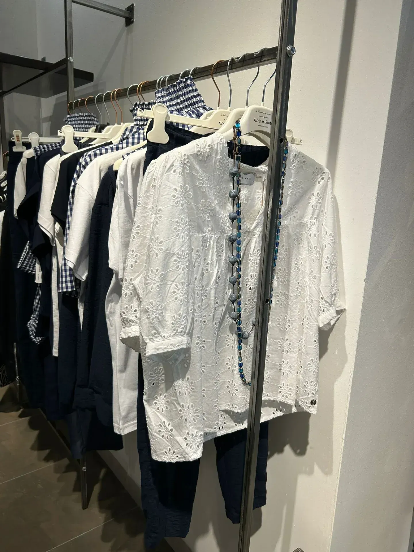 Appendiabiti con camicie bianche e blu navy, pantaloni e una collana di perline blu in un negozio.