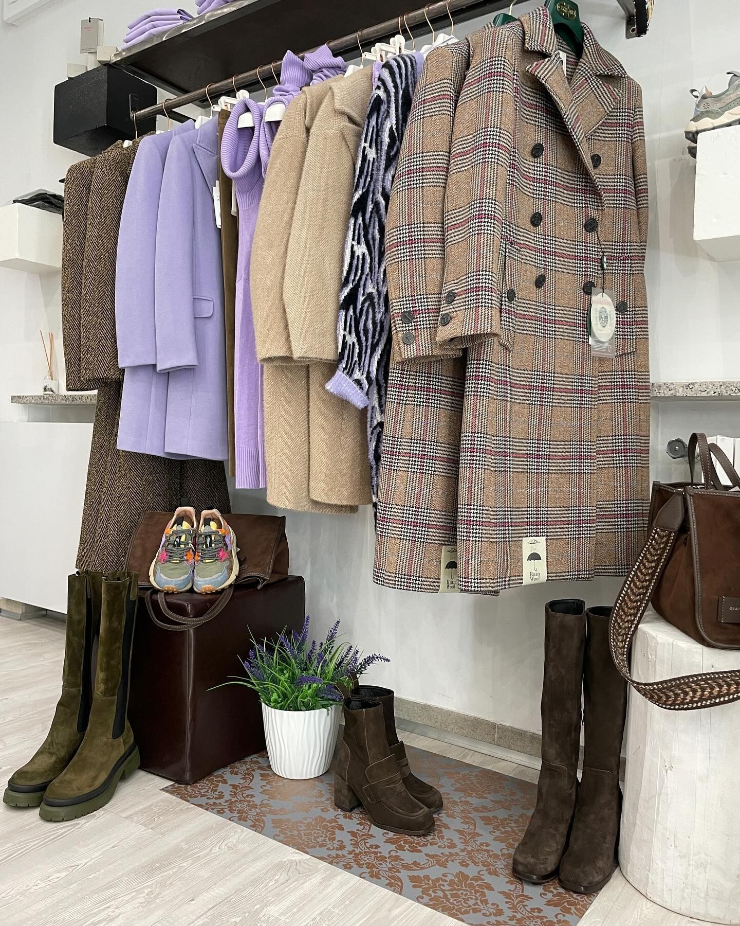 Appendiabiti in una boutique con cappotti, stivali e accessori nelle tonalità del marrone, lavanda e marrone chiaro.