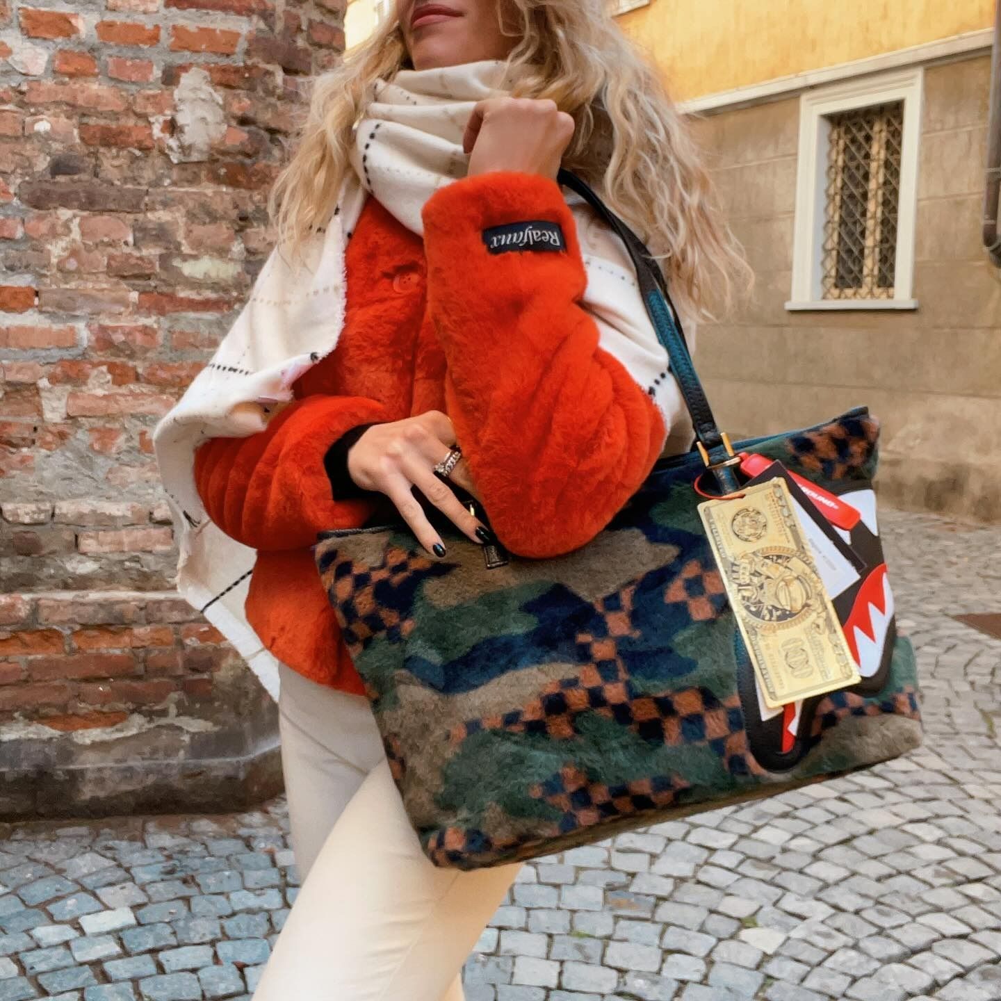 Donna con giacca di pelliccia arancione che tiene in mano una borsa mimetica, all'aperto.