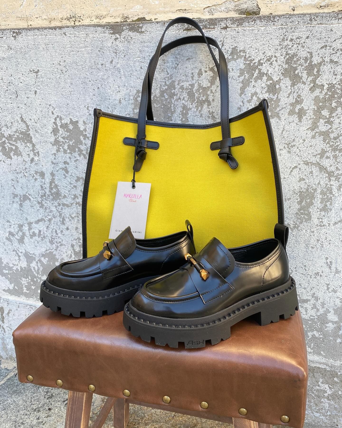 Borsa gialla e scarpe nere con suola carrarmato su uno sgabello.