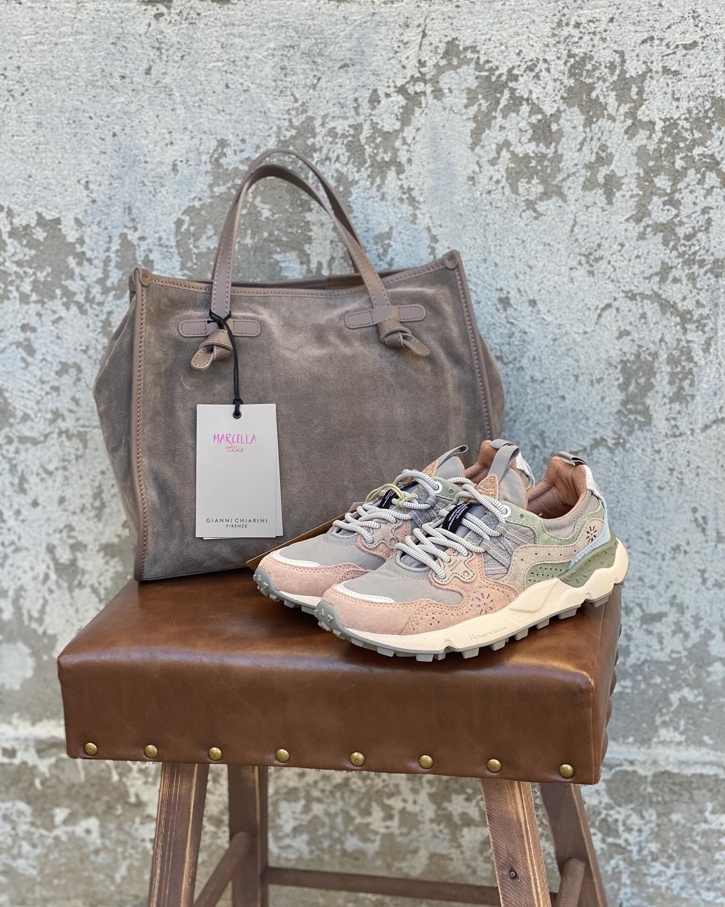 Una borsa tote in pelle scamosciata marrone chiaro e delle scarpe da ginnastica beige sono appoggiate su uno sgabello.