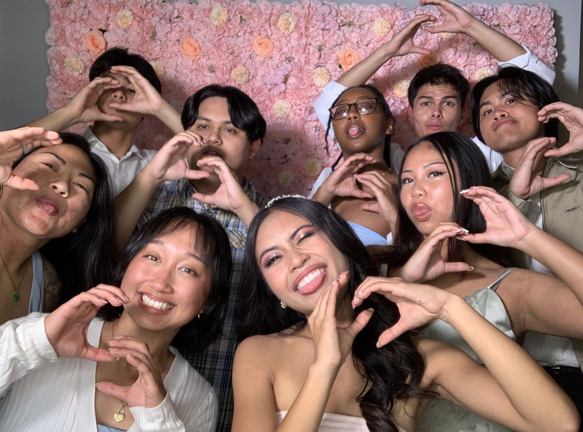 A large group posing for a photo against a multicolored background; some are smiling, making signs, or looking serious.