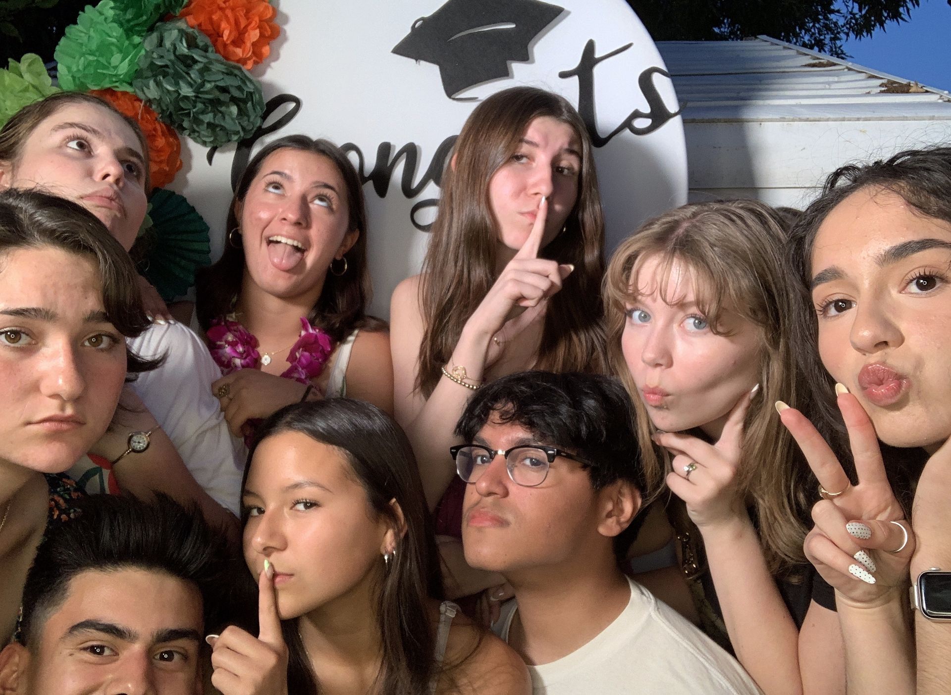 Group of people posing closely together at a party, making playful faces and peace signs before a photo booth backdrop