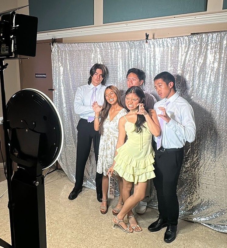 Five people pose for a photo in front of a silver sequined backdrop at an event.