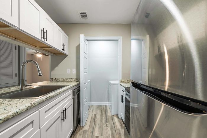White kitchen with stainless steel appliances and open doorway to a laundry area; light wood-look floors.