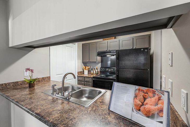 Kitchen with a sink, stove, fridge, and a cookbook open on the counter, featuring food.