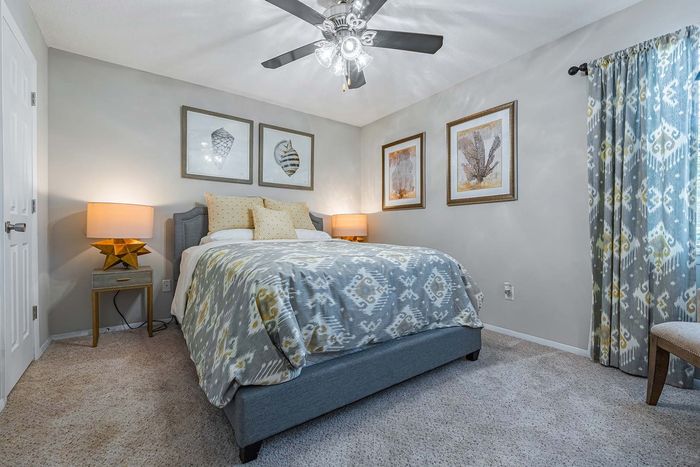 Bedroom with grey walls, bed, and patterned blue and yellow accents, lit by lamps and ceiling fan.