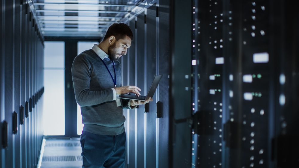 Man Using a Laptop in a Server Room is Surrounded by Racks of Computers — INtelephony In Albury, NSW