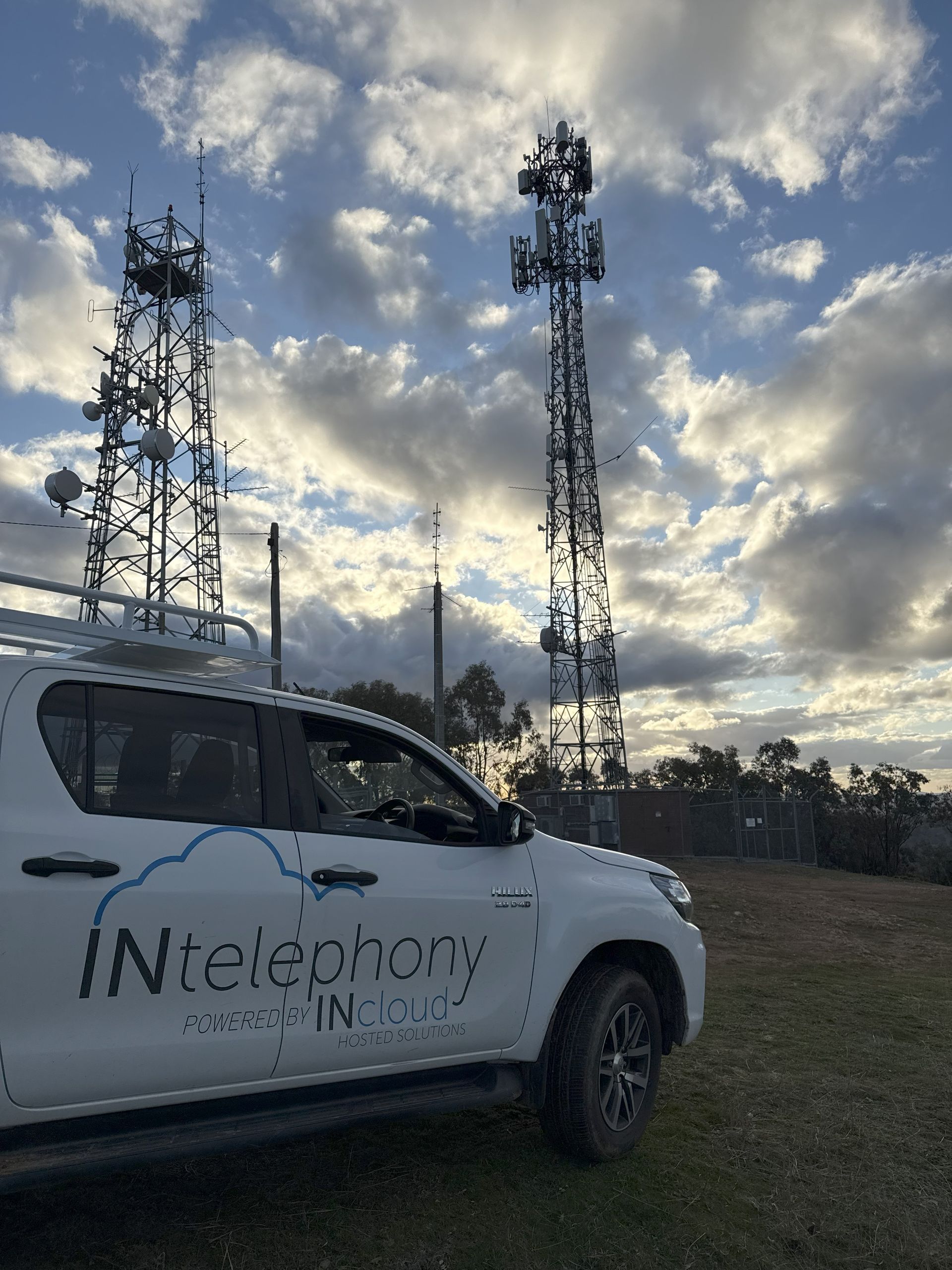 White INtelephony INC. Truck near two cell towers under a cloudy sky — INtelephony In Albury, NSW