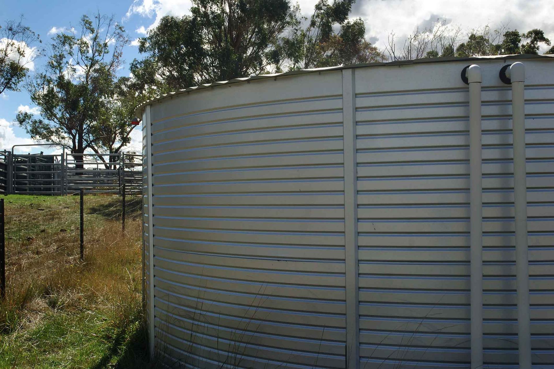 A large aluminum water tank is sitting in the middle of a grassy field.
