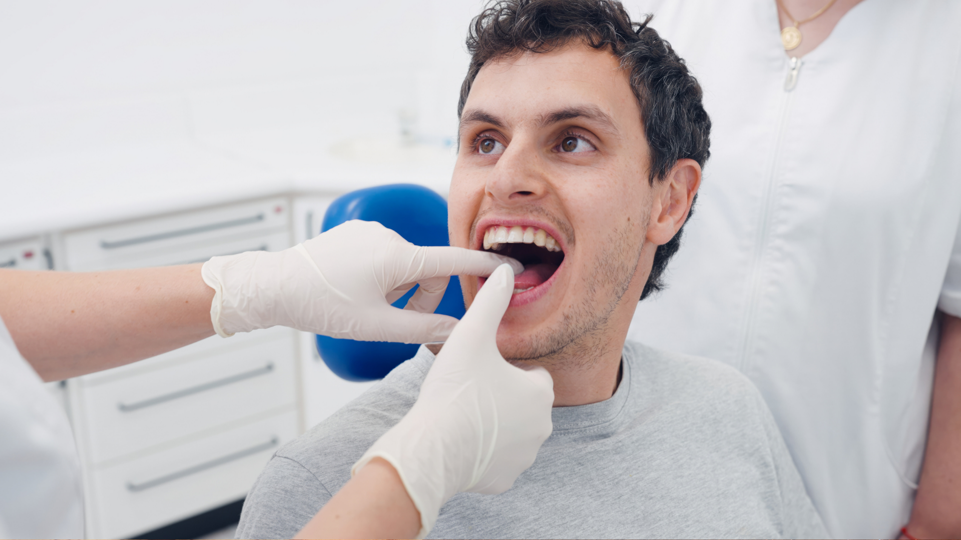 A dentist with gloved hands examines the teeth of a patient seated in a dental chair.