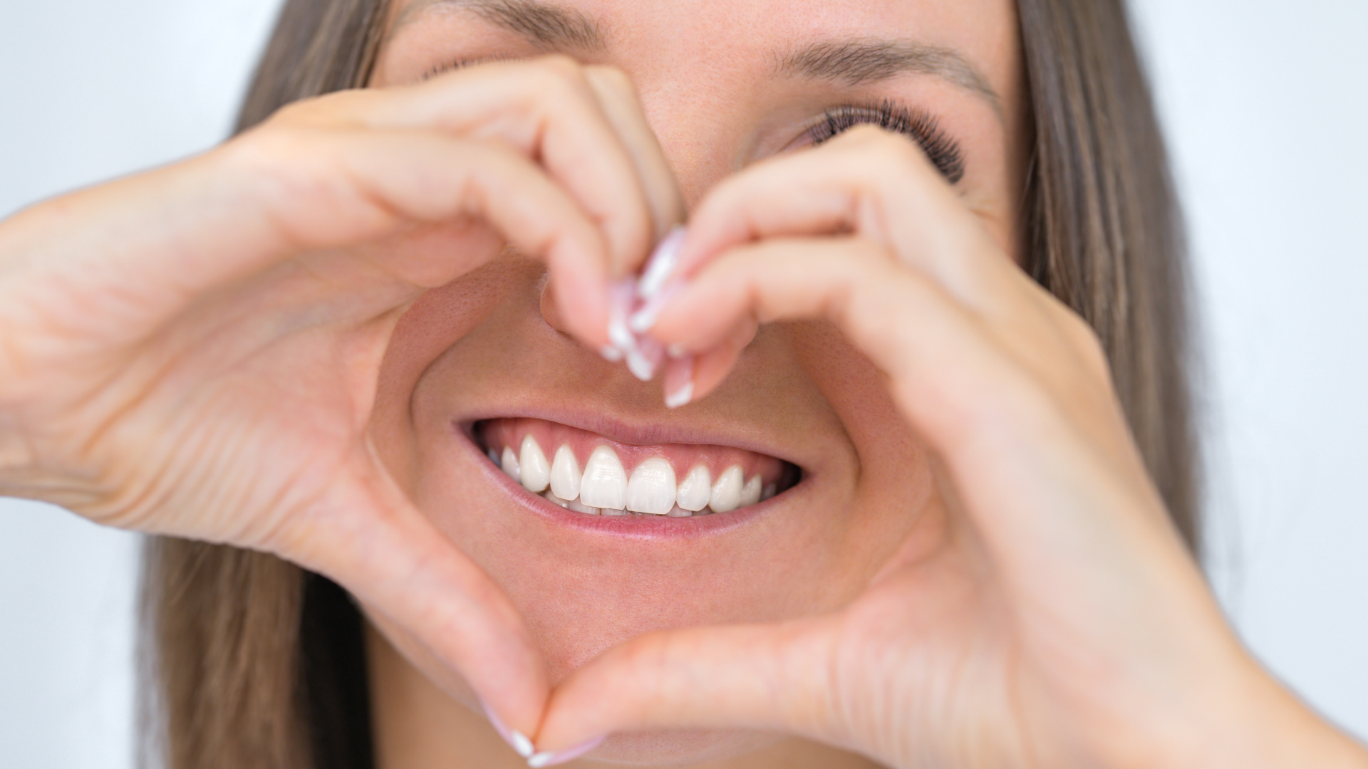 Hands forming a heart shape around a smiling mouth with white teeth