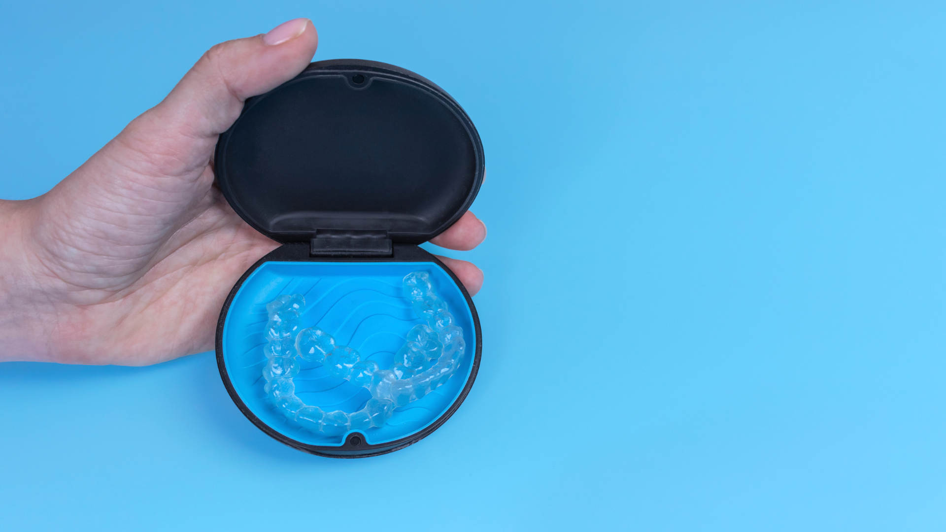 A person is holding a dental retainer in a case on a blue background.