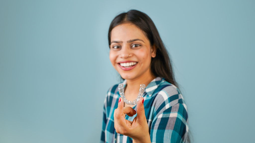 Woman smiling, holding clear dental aligners, blue background.