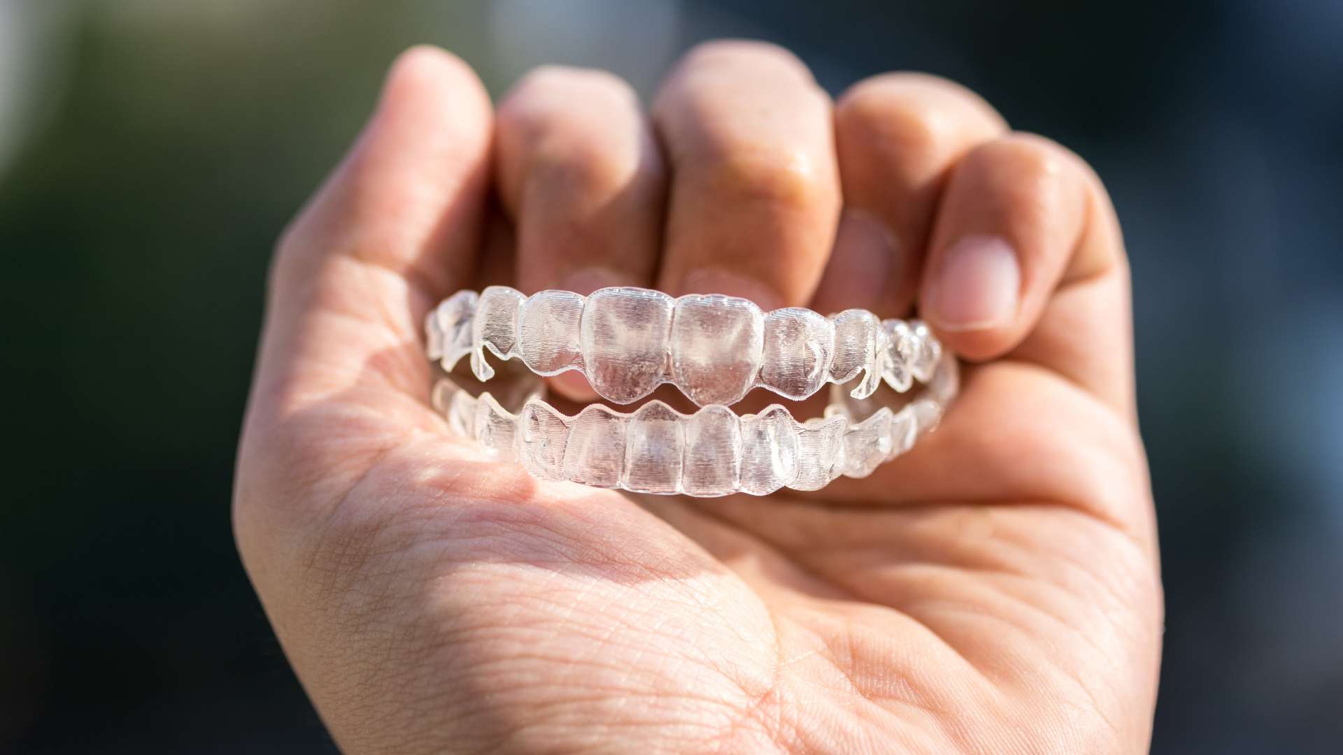 Hand holding clear Invisalign teeth aligners.