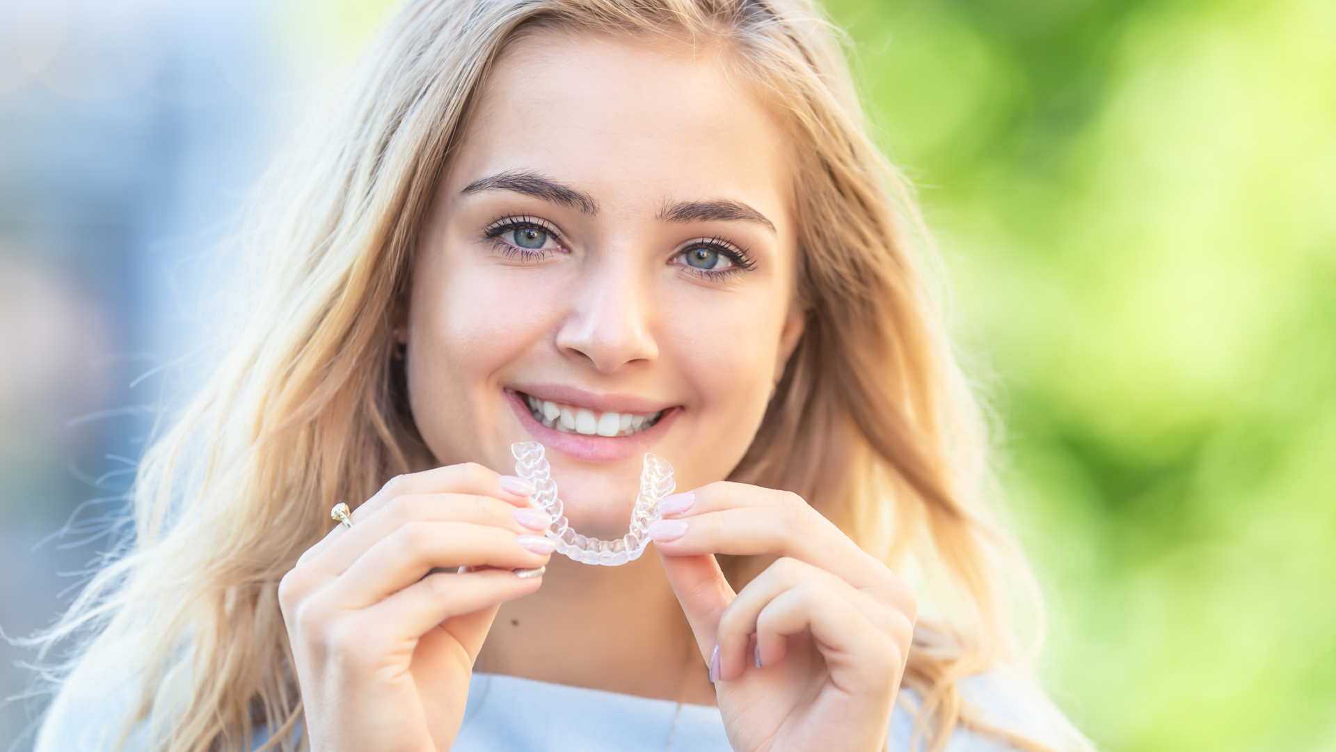 A woman is holding a clear retainer in her hands and smiling.