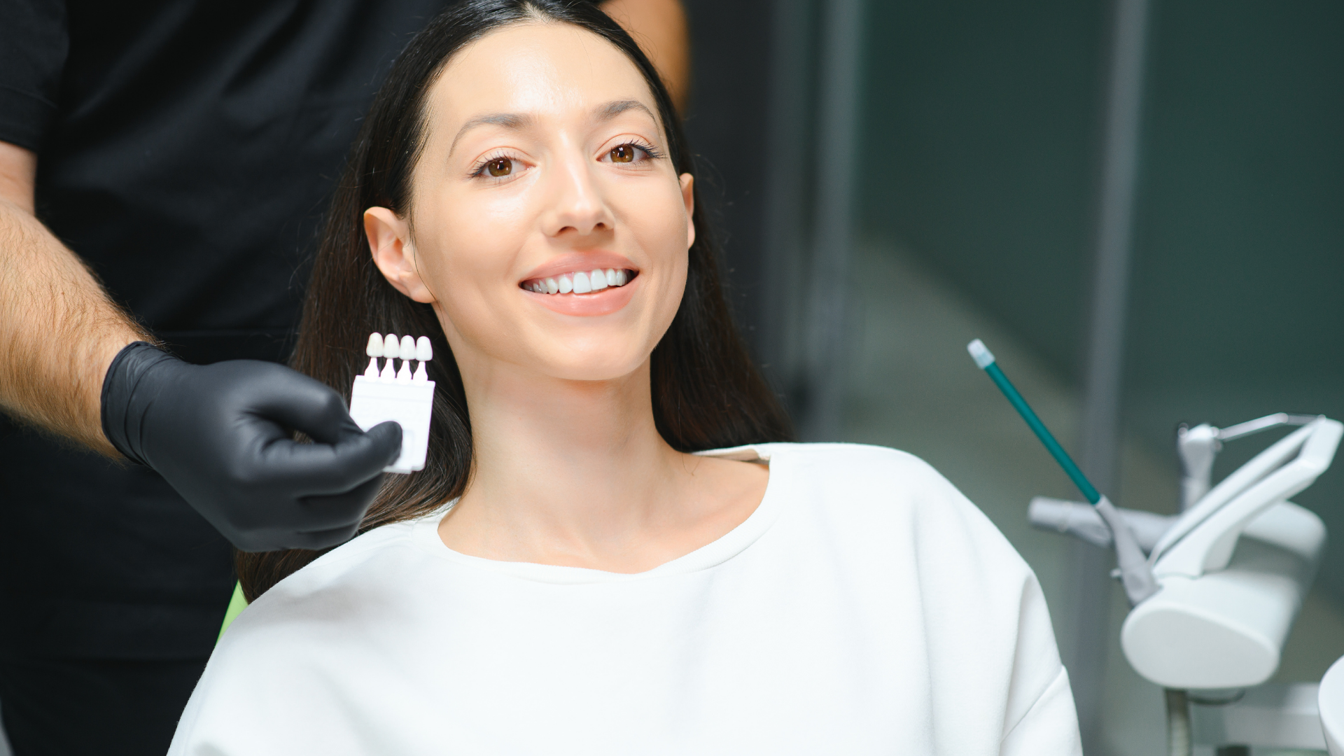 Woman holding clear aligner, smiling, wearing blue striped shirt against white background.
