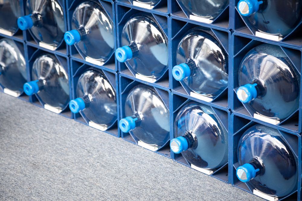 Blue Plastic Rack Holding Rows of Large, Clear Water Bottles With Blue Caps — Cool Blue Ice & Water in Taminda, NSW