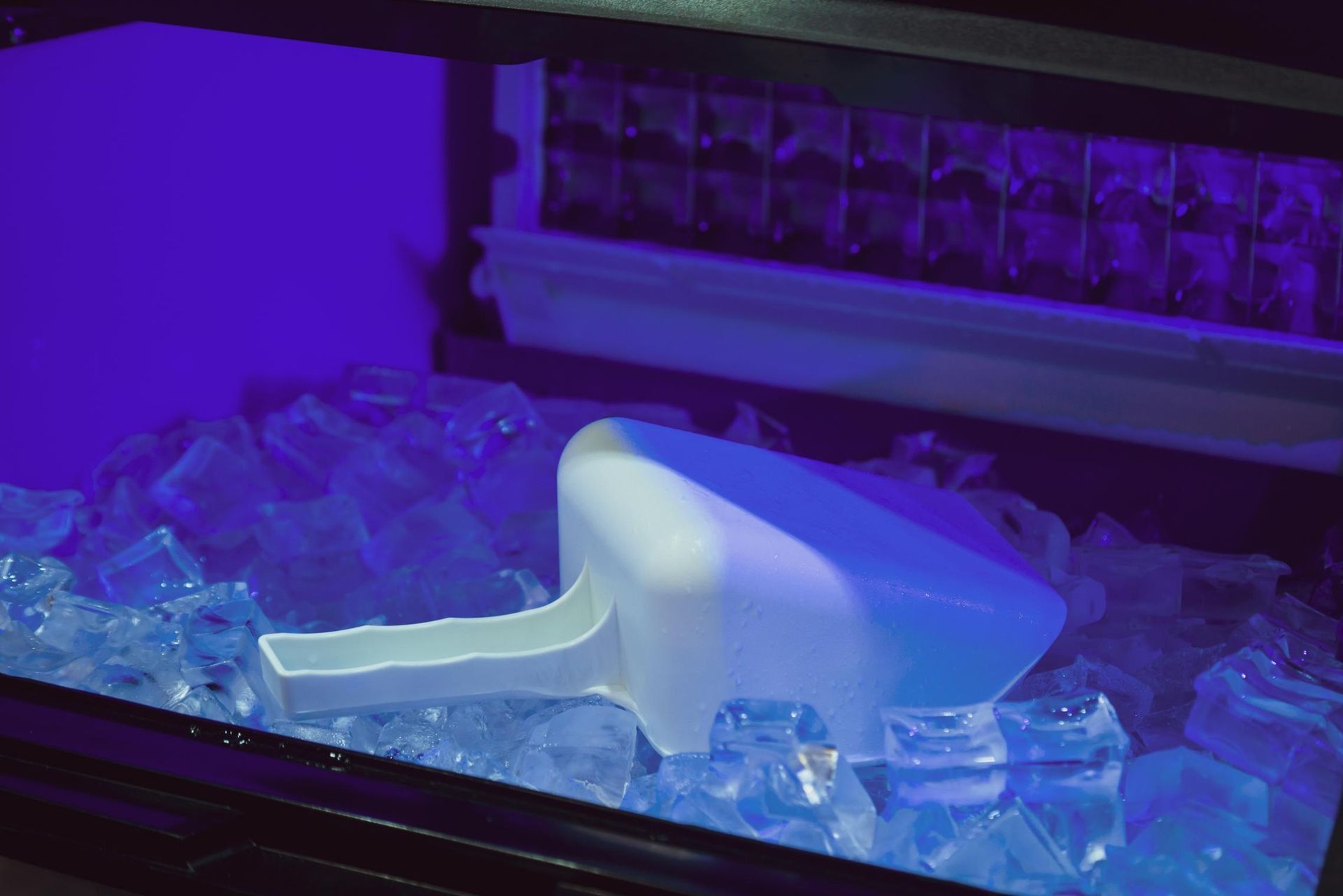 A Plastic Ice Scoop Rests in a Bin Filled With Ice Cubes — Cool Blue Ice & Water in Walgett, NSW