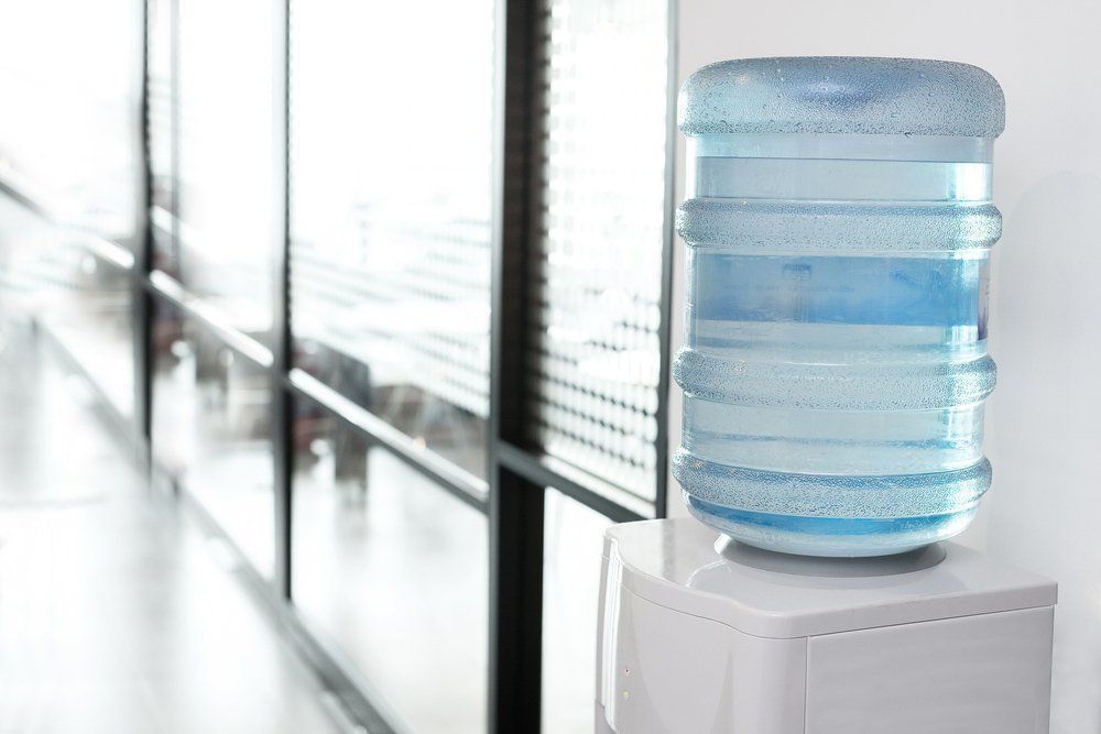 A Large, Clear Plastic Water Jug Sits Atop a White Water Cooler in a Hallway — Cool Blue Ice & Water In Lightning Ridge, NSW