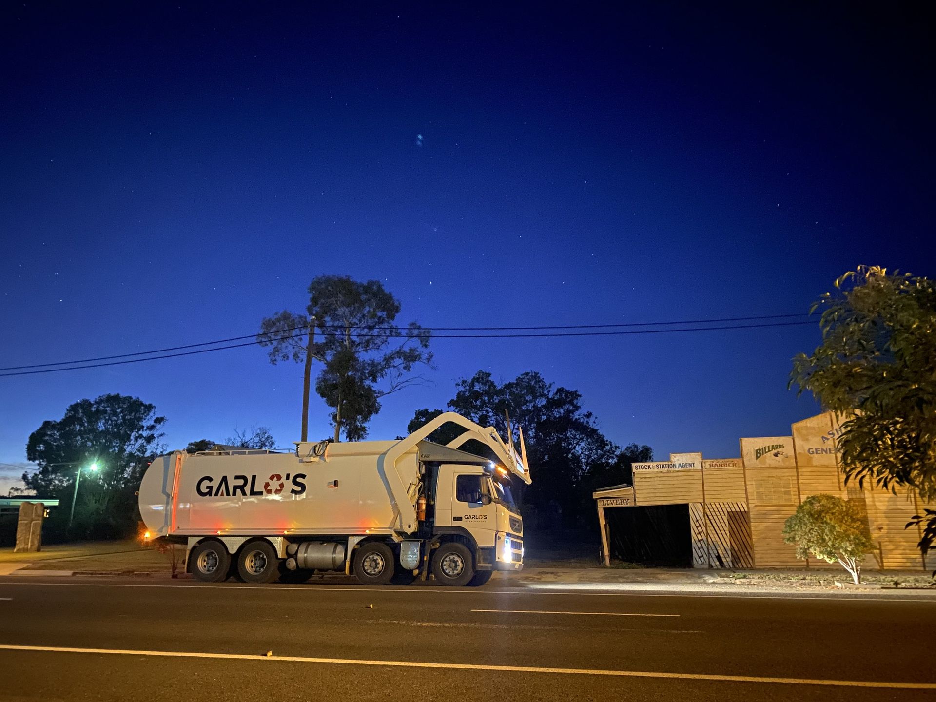 A garbage truck is loading a green trash can into it.
