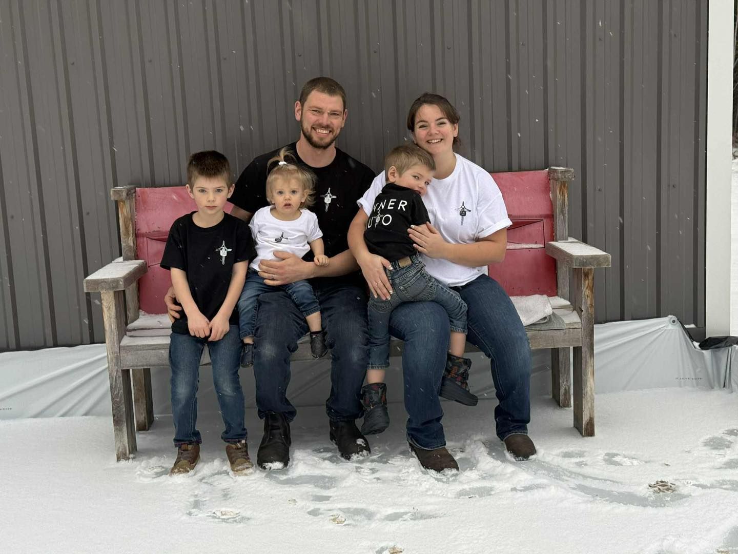 Family of five sits on a wooden bench in the snow; all wear matching shirts with a star logo.