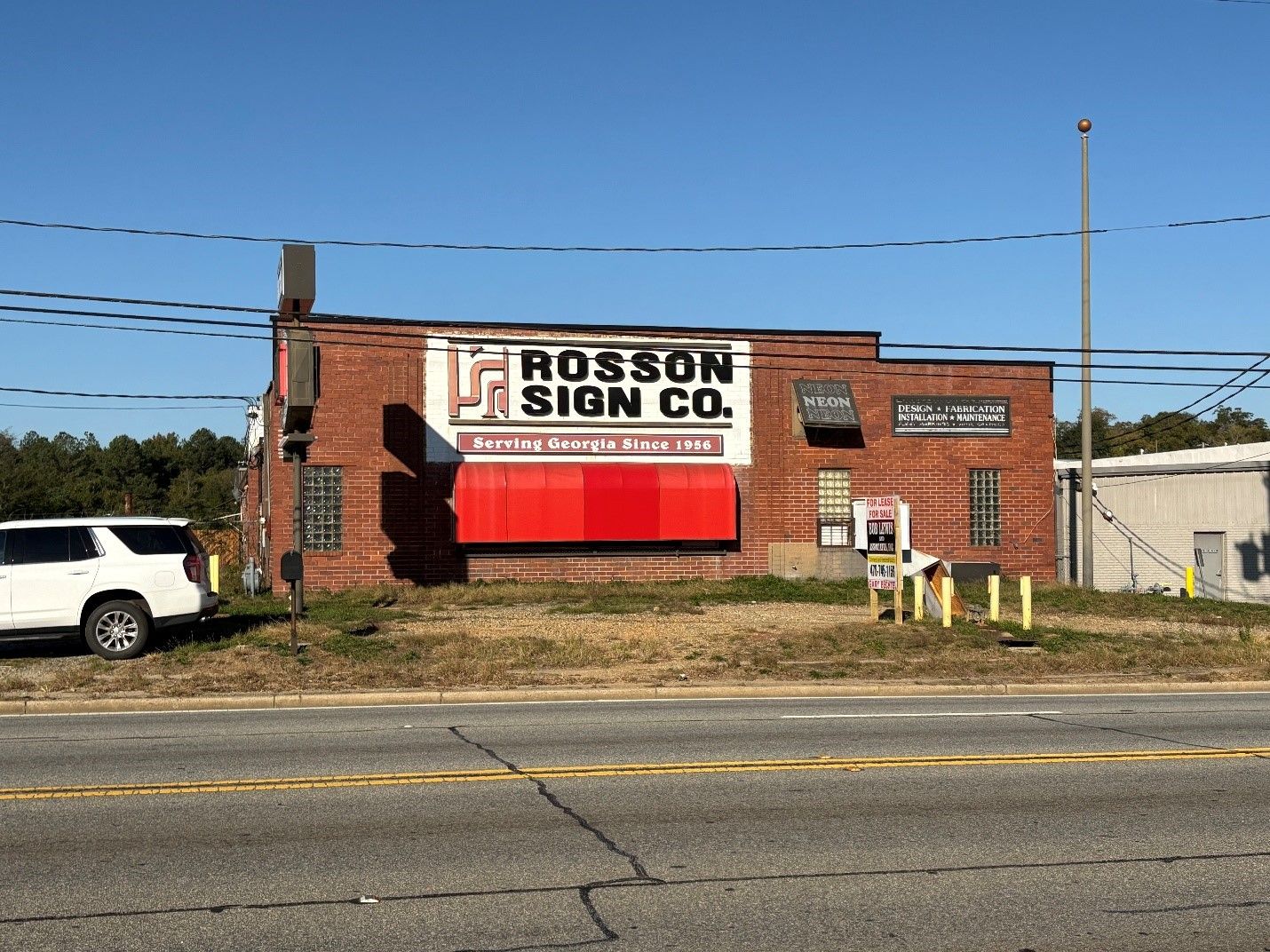 A white suv is parked in front of a rosson sign co. building