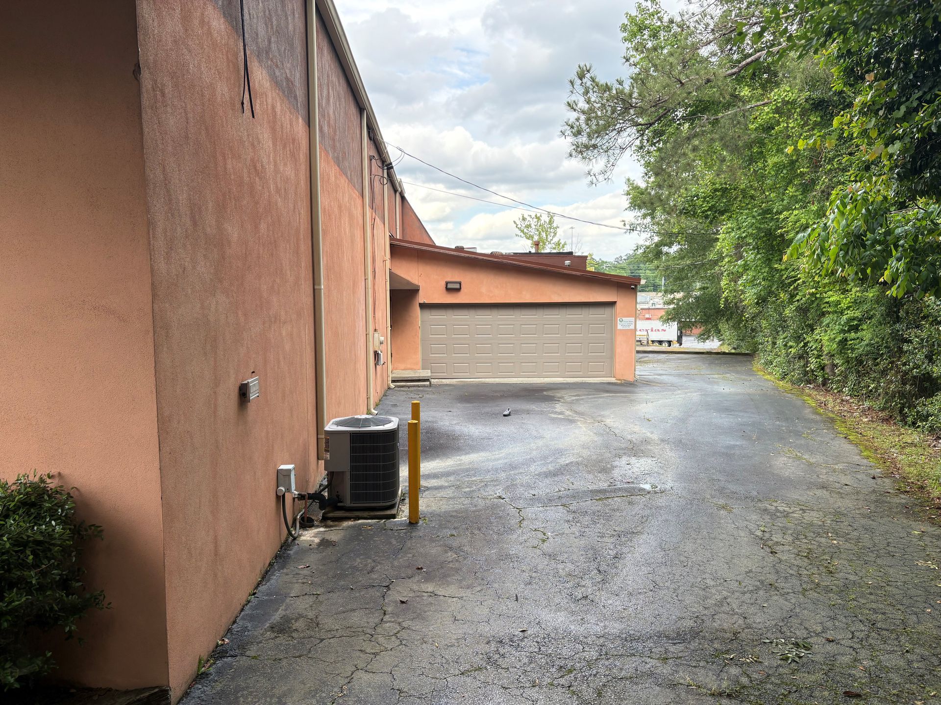 A driveway leading to a garage and a building with a lot of trees in the background.