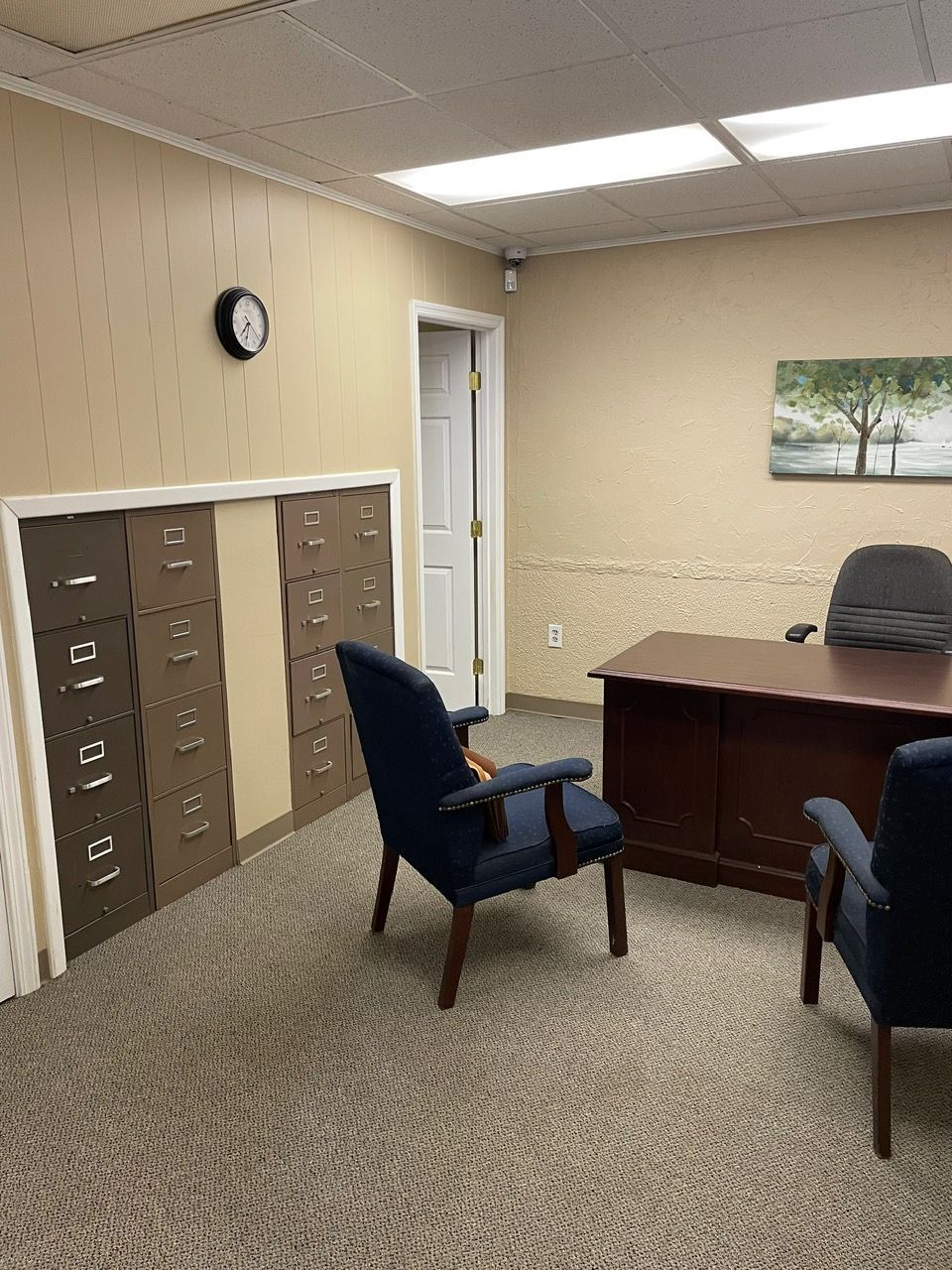 A room with a desk , chairs and a clock on the wall.
