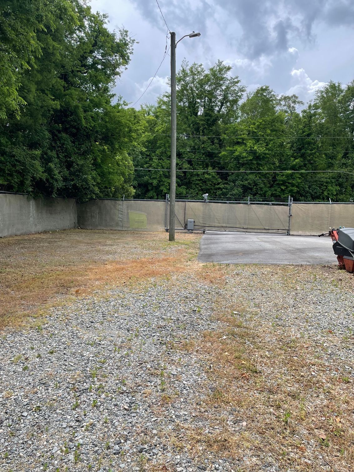 A gravel lot with a fence and trees in the background.