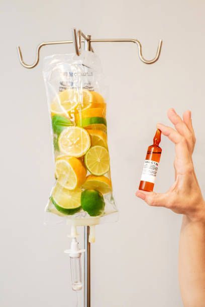 A person is holding a bottle of medicine next to a IV bag of lemons and limes.