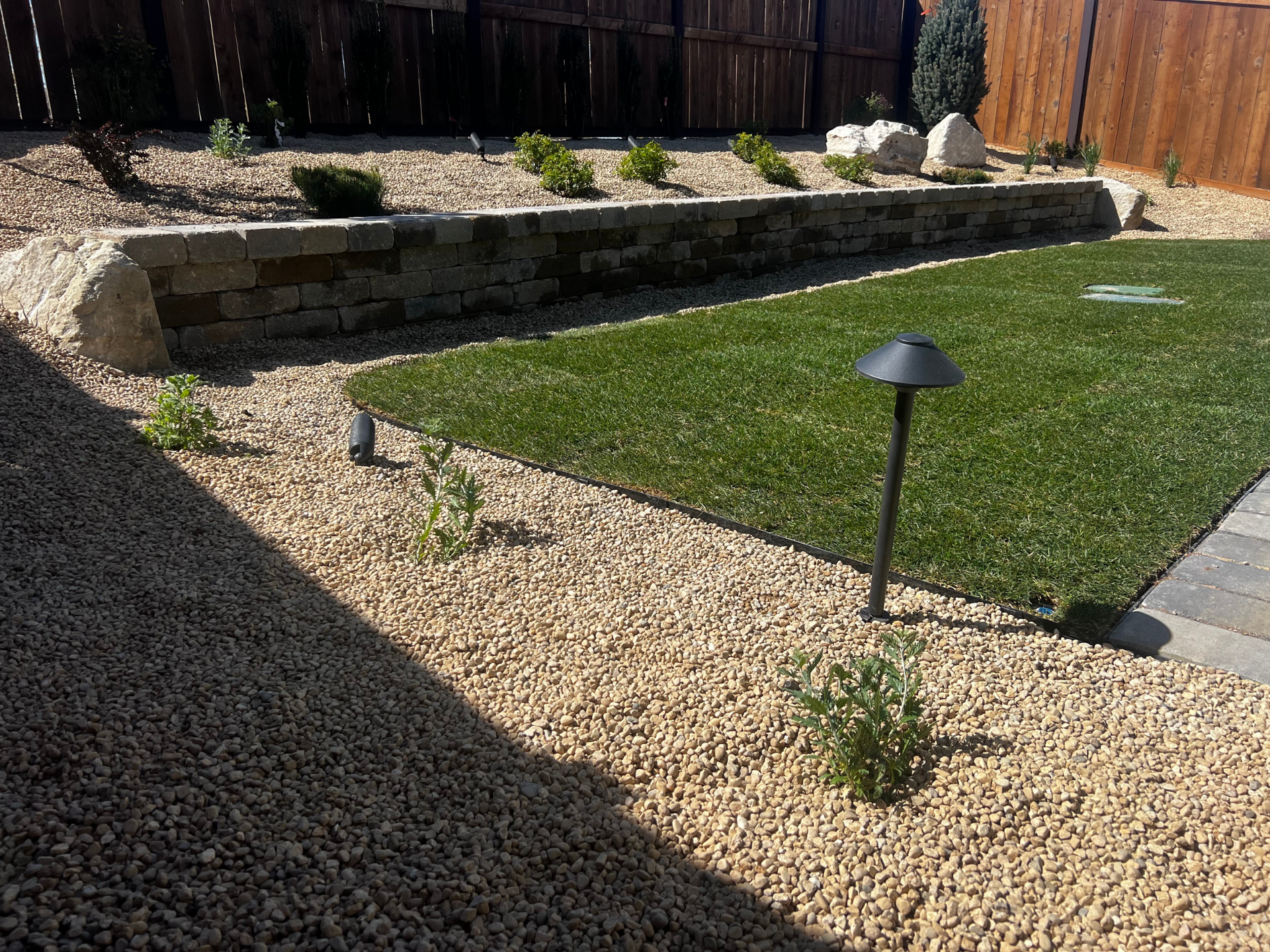 A backyard with a fence , gravel , grass and a few lights.