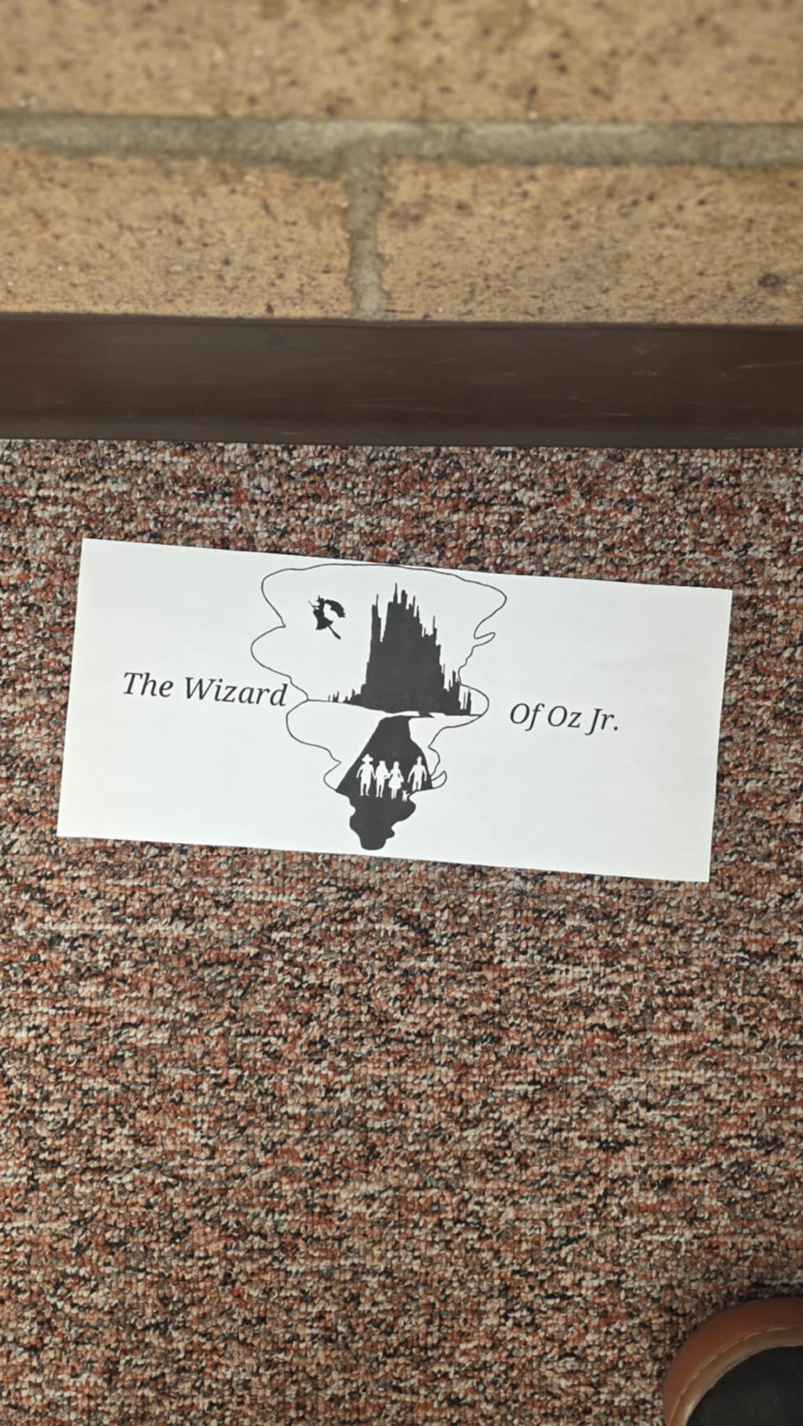 Hand-drawn art with a silhouette of a building and text on a white paper, resting on a brown patterned rug.