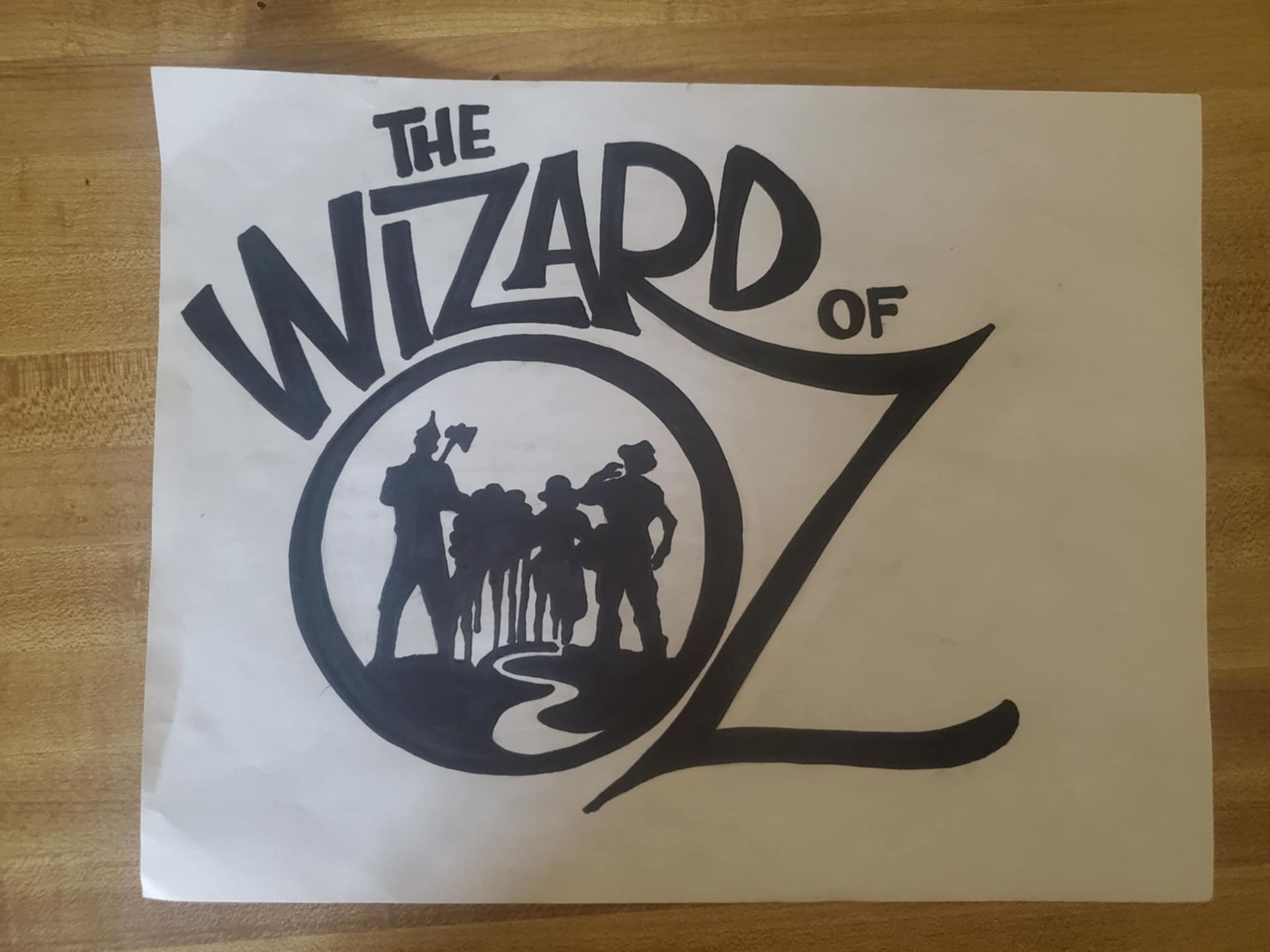 Black and white Wizard of Oz logo with characters in a circle and title text.