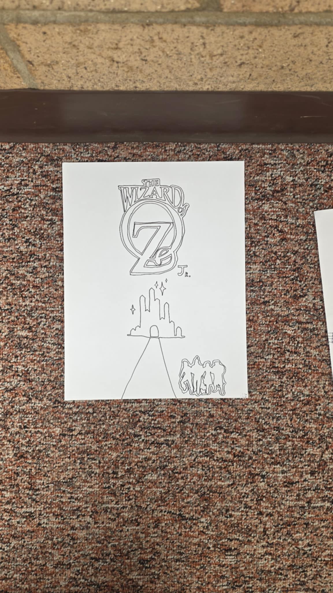 A drawing of a Z shape with lines, dots, and symbols, on a white paper, resting on brown carpet.