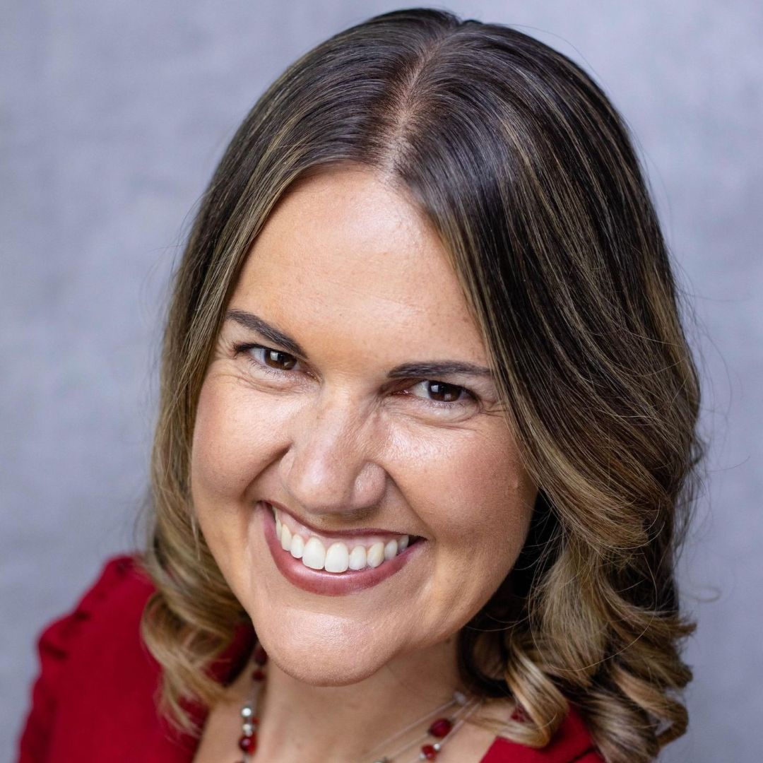 A woman in a red shirt and necklace is smiling for the camera.