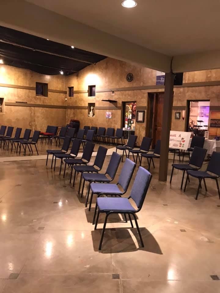 Rows of blue-upholstered chairs arranged in a large, brightly lit hall with textured tan walls and tiled floors.