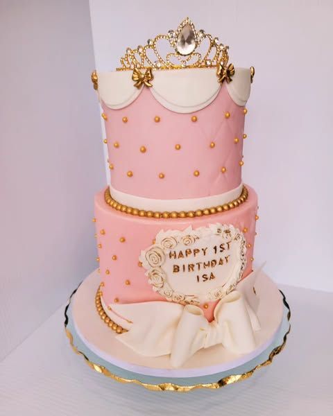 Two-tiered pink princess cake with gold accents, a tiara, and the words 