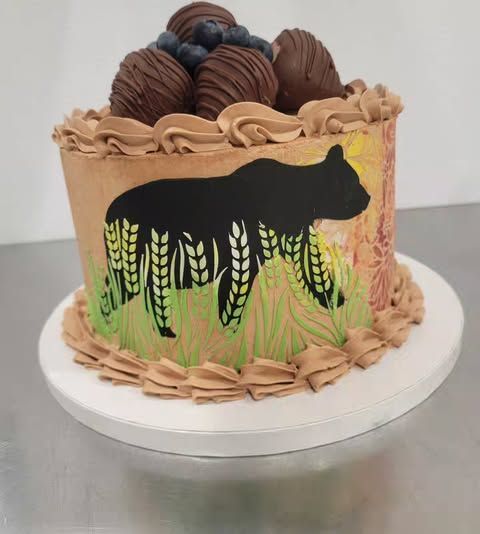 Cake decorated with a black bear silhouette, grass, and chocolate-covered strawberries.