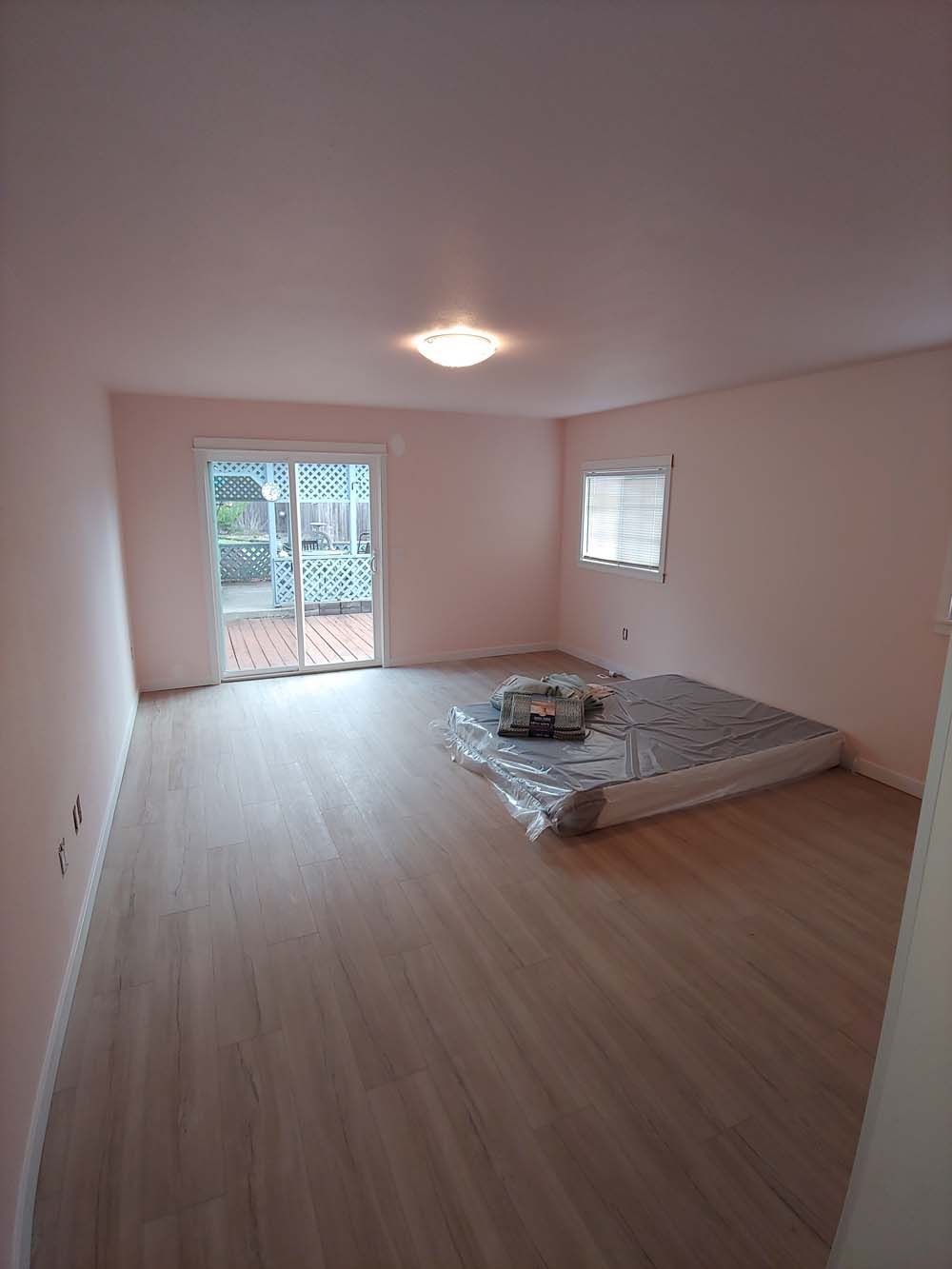 An empty room with a mattress on the floor and a sliding glass door.