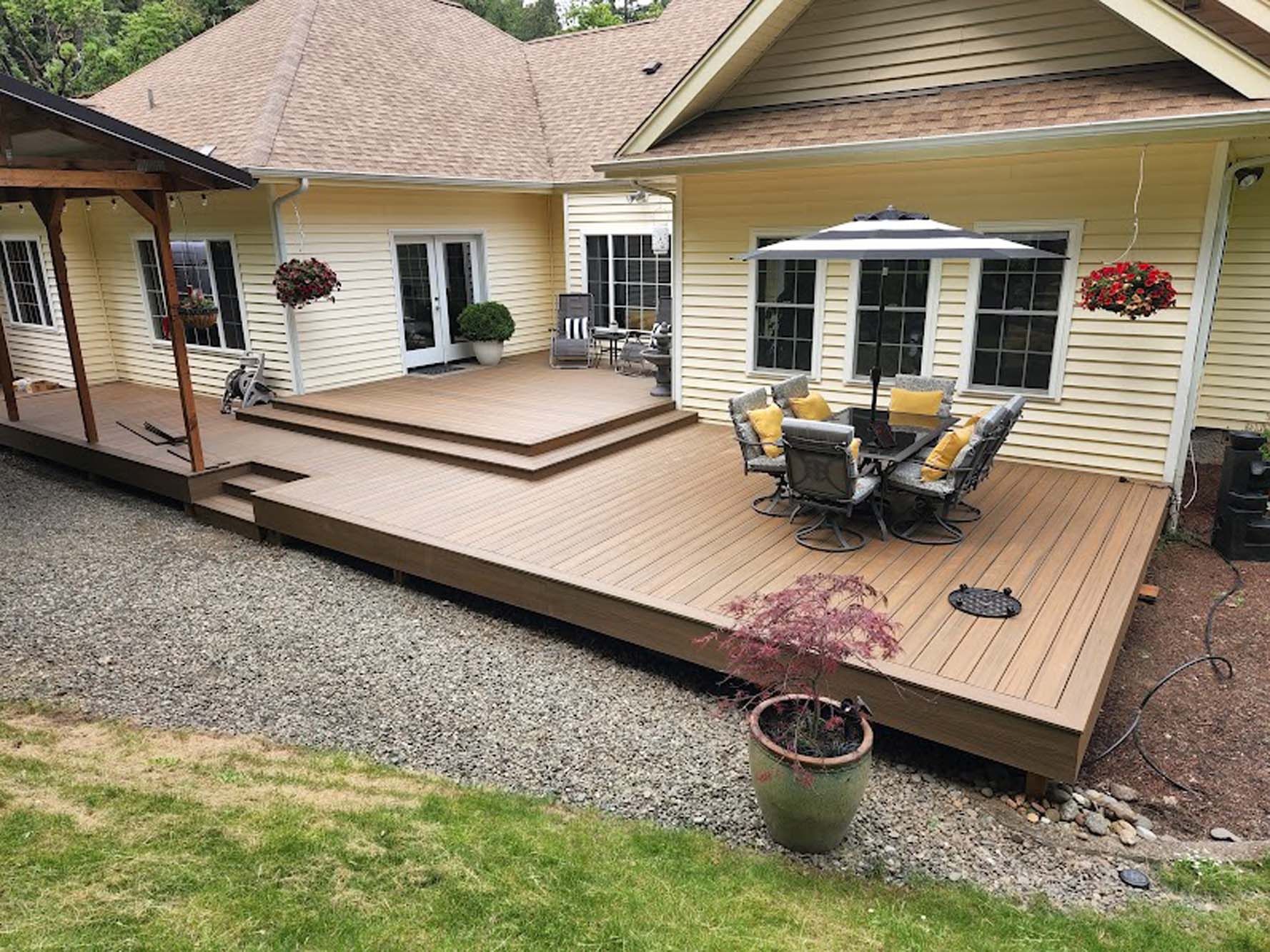 There is a large deck with a table and chairs on it in front of a house.
