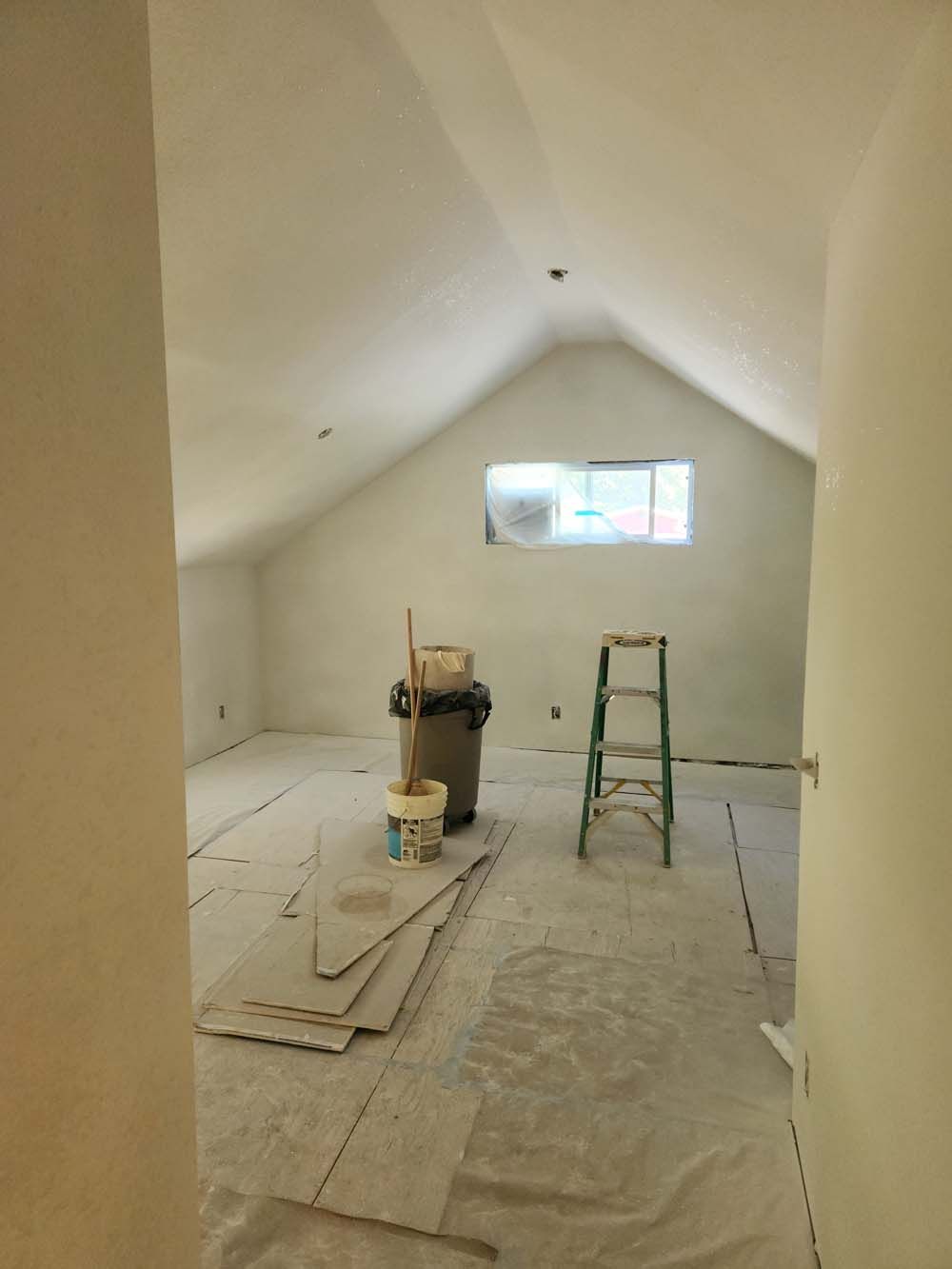 A room with a ladder and a trash can in it.