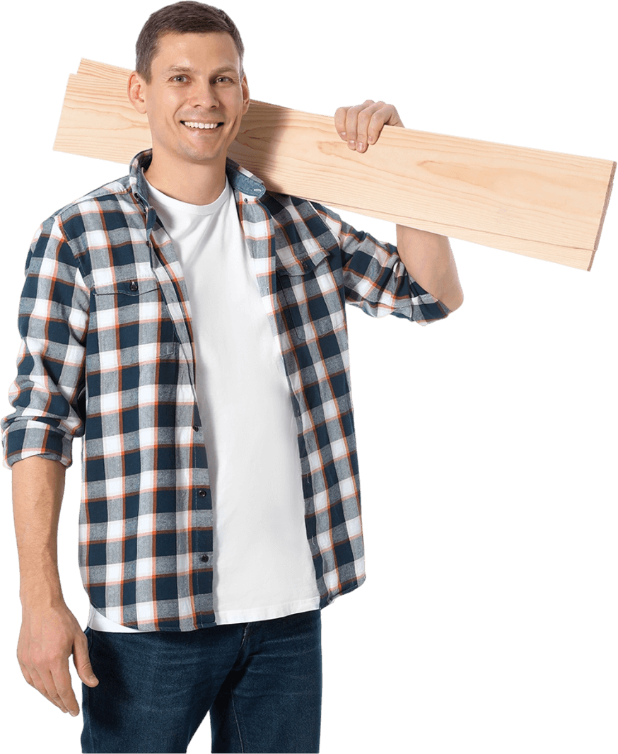 A man in a plaid shirt is carrying a large piece of wood on his shoulder.